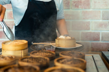 dim sum in bamboo steamer chinese cuisine. close up woman female hands holding tongs choosing meal...
