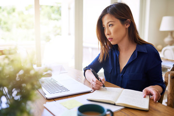 Young Asian businesswoman reading notes and working online from home