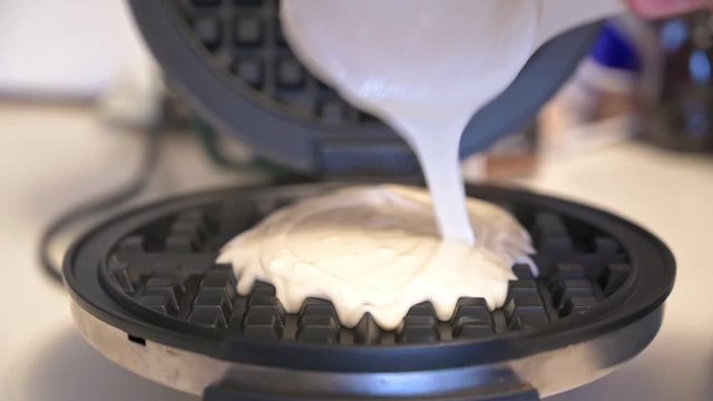 Pouring batter on to a waffle iron and closing the lid.