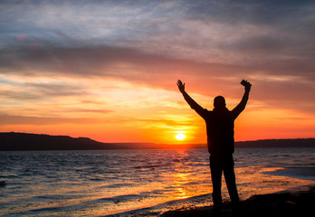 Fototapeta premium silhouette of a happy unrecognizable man at sunset on the lake