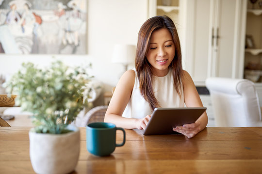 Smiling Asian woman sitting at home using a digital tablet