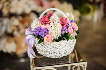 White basket with purple roses, white hyacinth and juicy pink orchids on the table