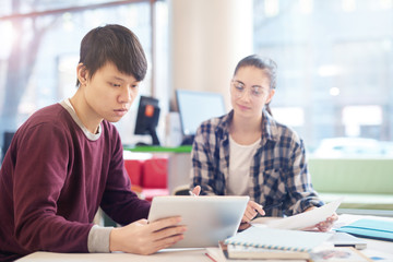 Asian young man studying and using digital tablet while sitting at the table together with young woman