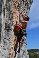 Young strong man with large muscles does rock climbing in Finale Ligure, Italy. Sunny day, blue sky.
