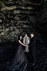 Fototapeta premium wedding ceremony in a black cave on a black sand beach in Iceland near the Atlantic Ocean. Bride in black dress groom in black clothes