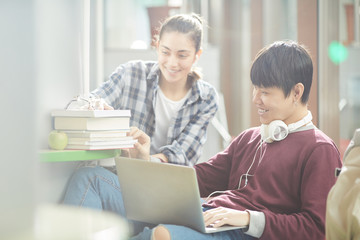 Asian young man sitting and using laptop with young woman who bringing the books and helping him in study