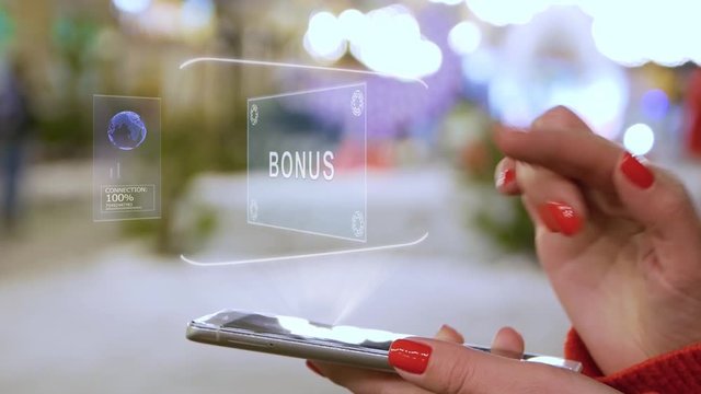 Female hands interact with HUD hologram text Bonus. Woman with red nails and sweater uses the holographic technology of the future in the smartphone screen on the background of street