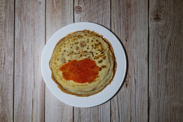 Stack of pancakes with red caviar on wooden background