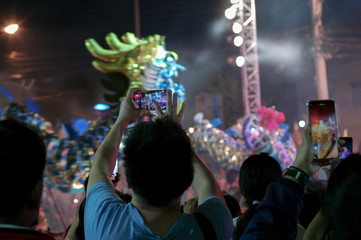 Selective focus on hands hold the mobile phone and record the clip of show with motion blurred dancing dragon performance in background