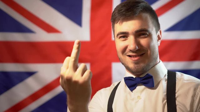 The arrogant British man shows an indecent gesture against the background of the flag of Great Britain. A gesture of excellence in the UK. Not a gentleman.