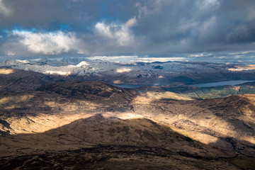 Dramatic winter view from Ben Lomond towards Loch Lomond and the peaks of Arrochar Alps in Scottish Highlands.