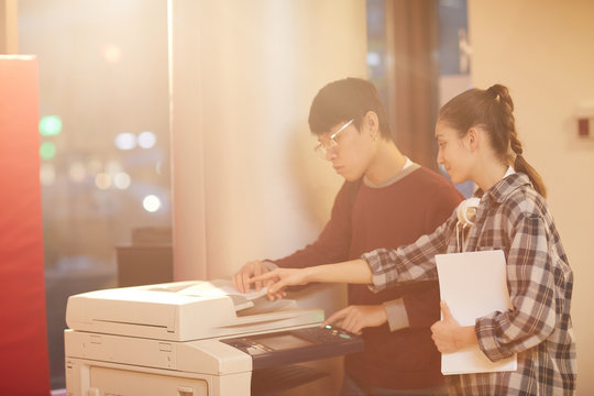 Young woman helping her friend to make the copy while they using copy machine at the university