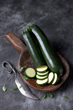 Courgette on wooden spoon with knife on black textile, close up