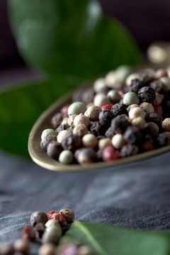 Brass spoon with peppercorns and leaves on textile, close up