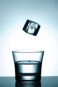 Water glass with flying icecube above the glass, motion blur on the cube