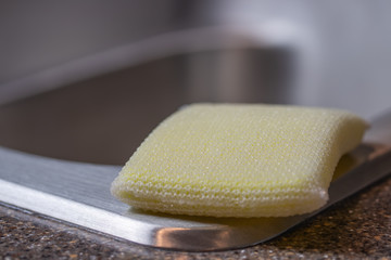 yellow sponge sitting on the edge of a stainless steal sink isolated macro shot with bokeh background 