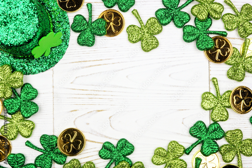 Wall mural St Patricks Day frame of green shamrocks, gold coins and leprechaun hat. Top view over a white wood background. Copy space.