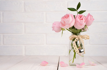 Bouquet of pink roses in a transparent glass vase with a ribbon and a metal heart on a white...