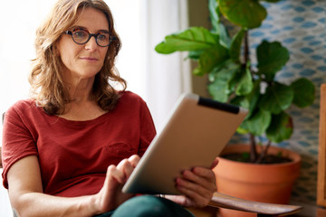 Mature woman sitting at home using a digital tablet