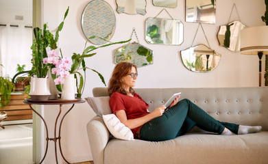 Mature woman using a tablet while lying on her couch
