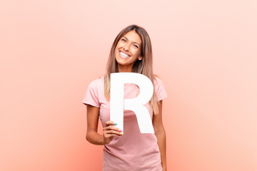 young pretty woman excited, happy, joyful, holding the letter R of the alphabet to form a word or a...