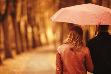 rain in the autumn park / young 25 years old couple man and woman walk under an umbrella in wet rainy weather, walk October lovers