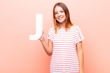 young pretty red head woman excited, happy, joyful, holding the letter J of the alphabet to form a...