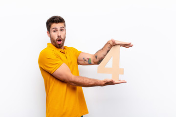 young handsome man surprised, shocked, amazed, holding a number 4.