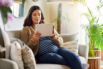 Young pregnant woman using a tablet in her living room