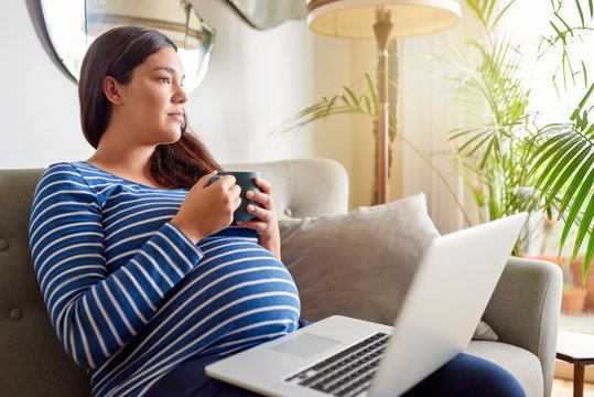 Young pregnant woman relaxing with a laptop and tea