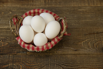 Close-up organic white eggs in a basket with a decorated checkered napkin on a wooden rustic background. Farm products. Easter holiday.
