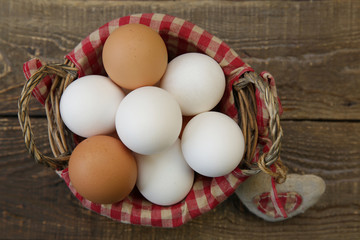 Close-up organic eggs in a basket with a decorated checkered napkin and a heart made of linen fabric on a wooden rustic background. Farm products. Easter holiday. Top view. Flat lay.