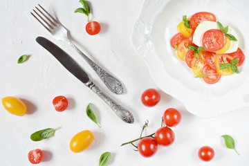 Fresh colorful tomatoes and basil salad on a white background. Fresh tomatoes with basil leaves in a ceramic bowl. Home made food. Concept for a tasty and healthy appetizer, flat lay. Caprese