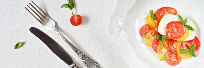 Fresh colorful tomatoes and basil salad on a white background. Fresh tomatoes with basil leaves in a ceramic bowl. Home made food. Concept for a tasty and healthy appetizer, flat lay. Caprese