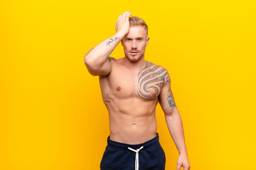 young strong blonde man raising palm to forehead thinking oops, after making a stupid mistake or...