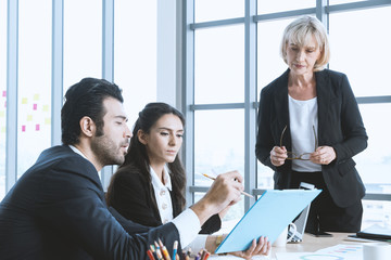 Businessman had pointing at report and give a advice to colleague with boss standing and listening a report at modern office building. Consultant business concept.