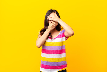 young latin pretty woman covering face with both hands saying no to the camera! refusing pictures...