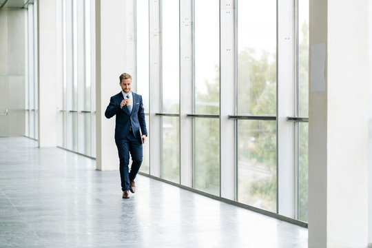 Businessman holding takeaway coffee walking at the window - Powered by Adobe