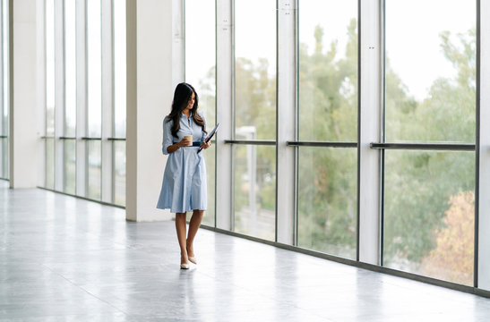 Businesswoman with tablet and takeaway coffee walking at the window