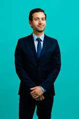 smiling portrait of a young entrepreneur business man smiling with both hands in front of his body,  isolated on blue studio background