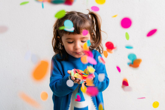 Happy little girl blowing the confetti at a party in front of a white wall