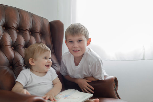 Portrait of boy with his baby brother in leather armchair in living room at home