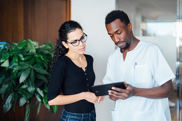 Dentist with tablet speaking with female patient in dental surgery
