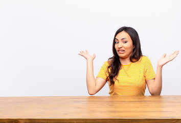 young latin pretty woman shrugging with a dumb, crazy, confused, puzzled expression, feeling...