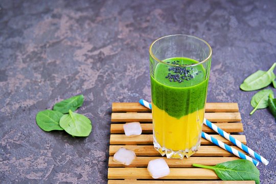 A healthy drink, a two-layer smoothie with fresh spinach and ripe mango in a tall glass glass on a dark concrete background. Drinks for detox and weight loss. Copyspace