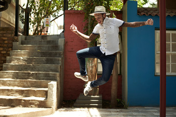 Portrait of young man with vitiligo wearing a hat, jumping in the street
