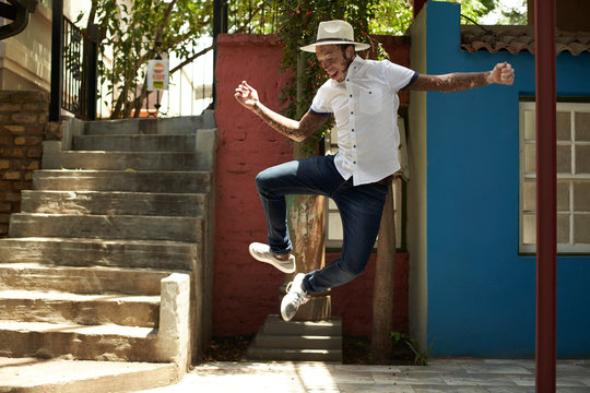 Portrait of young man with vitiligo wearing a hat, jumping in the street