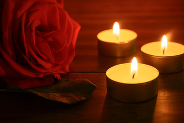 Fototapeta na wymiar a red rose lies on a table and three candles are burning