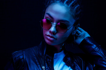 portrait of an African American young woman in sunglasses isolated on a black background in neon...