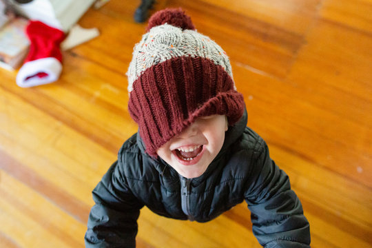 Smiling toddler boy wearing winter hat laughs with eyes covered by hat